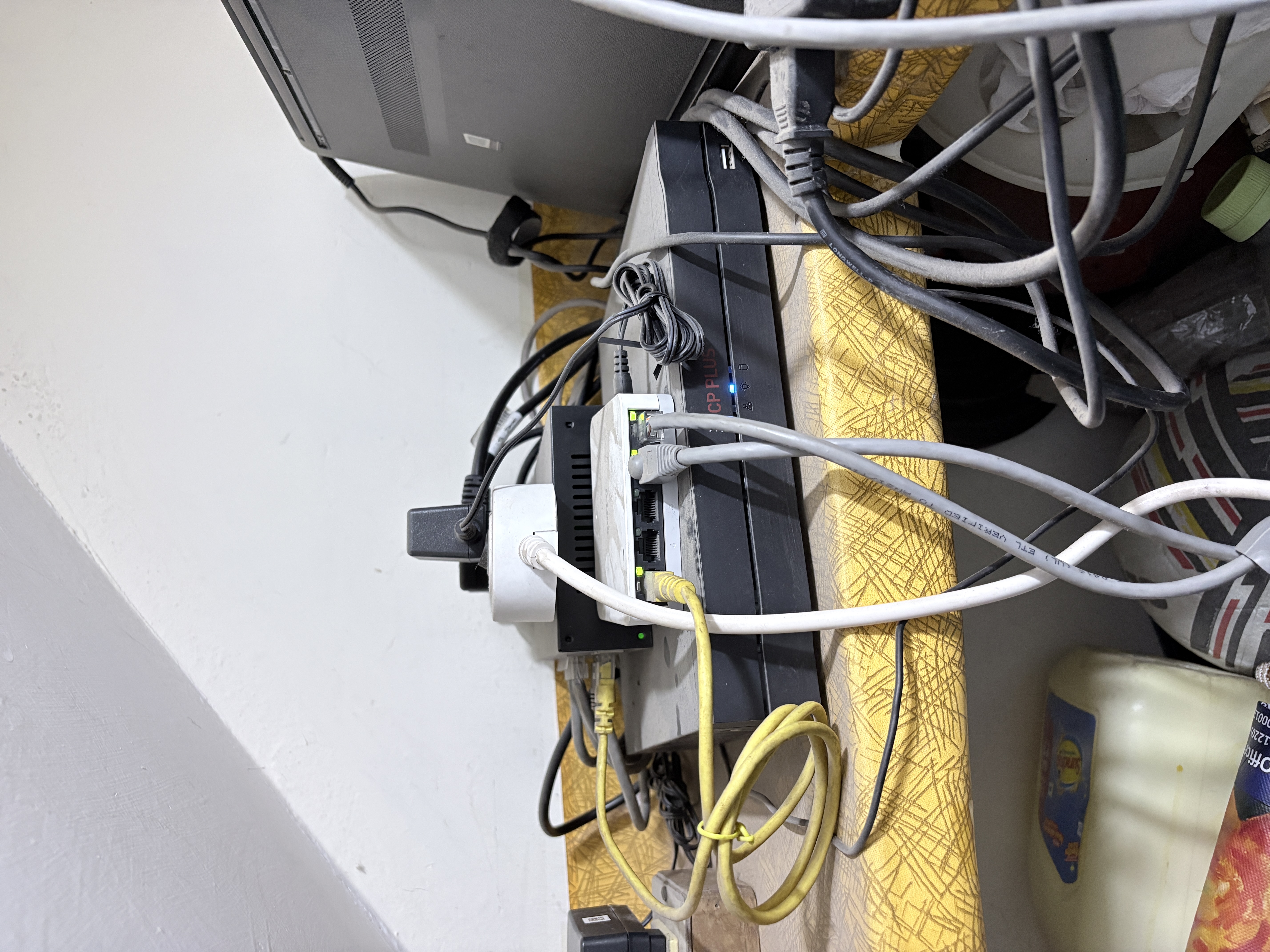The shelf under the stairs — switch, router, cables, and the sloped ceiling that defines the datacenter